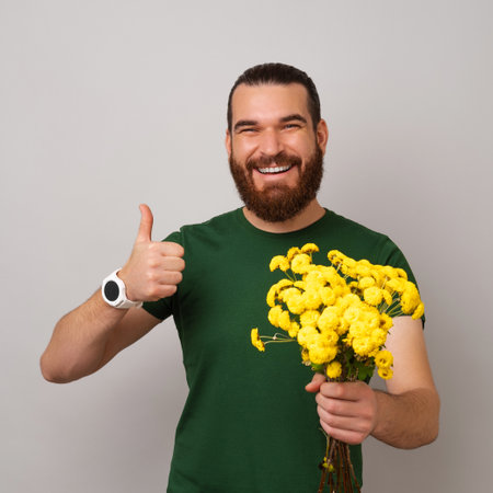 Smiling man is holding a bunch of yellow flowers and showing thumb up.の写真素材