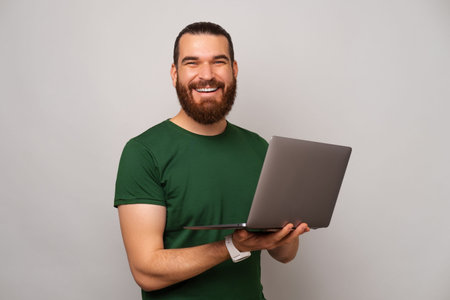 Handsome strong man is holding his opened laptop while typing something.の写真素材