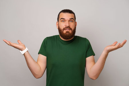 Confused young bearded man is shrugging his shoulder because he does not know.