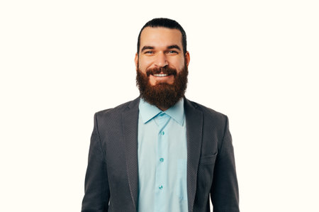 Portrait of young handsome bearded man in casual suit looking and smiling at camera isolated on whiteの写真素材