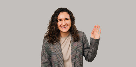 Photo of charming happy young woman in casual suit making Hello gesture over grey background