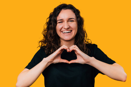 Close up portrait of a laughing woman showing heart gesture over her chest.