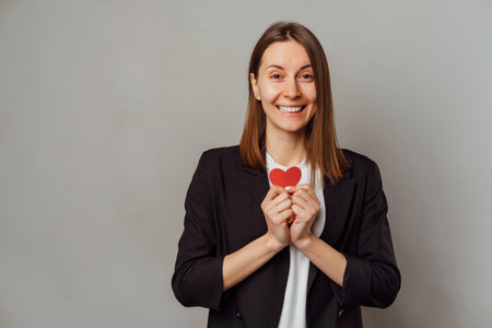 Excited smiling woman wearing jacket holds a little red heart over her chest.の写真素材