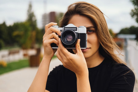 Beautiful young woman is taking a photo with a vintage camera outdoors.の写真素材