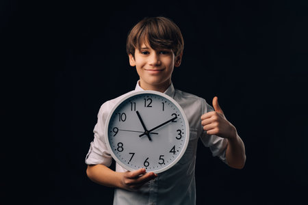 Smiling young teen boy is holding a round clock while showing thumb up.の写真素材