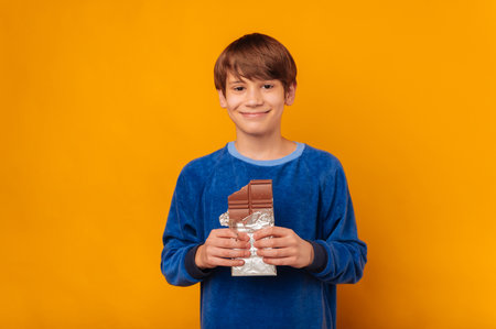 Handsome smiling young teen boy is holding a bitten bar of milk chocolate.の写真素材
