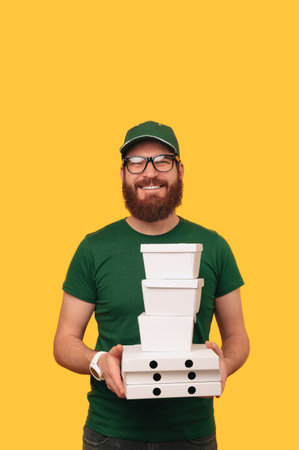 Vertical shot of a delivery smiling man in green holding some lunch boxes.の写真素材