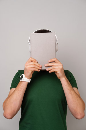 Man covering his face with a journal or book cover while wearing headphones.の写真素材