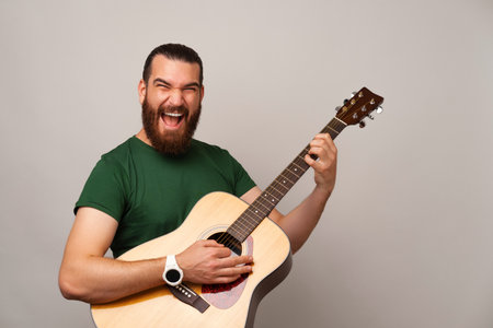 Ecstatic young bearded man is holding and playing rock on an acoustic guitar.の写真素材