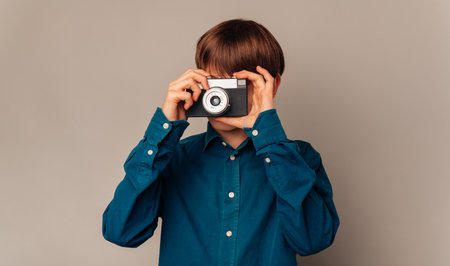Handsome teen boy in blue shirt is looking through his old vintage camera.の写真素材