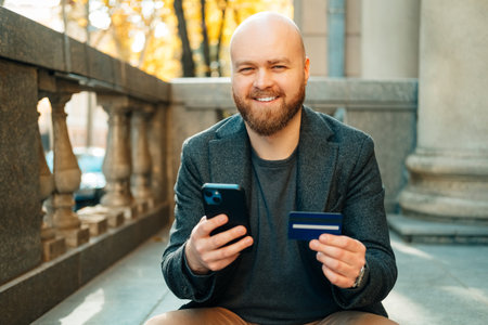Cheerful bald man is using his mobile banking while holding phone and card.の写真素材