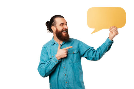 Handsome ecstatic bearded hipster man is pointing at a yellow speech bubble.
