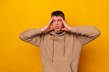 Photo of young man standing over yellow background and having some headacheの写真素材