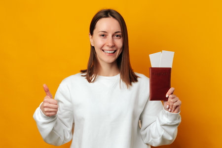 Wide smiling woman is holding a thumb up and her passport with some tickets.の写真素材