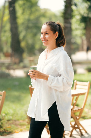 Young woman wearing white shirt is walking and enjoying her morning coffee.の写真素材