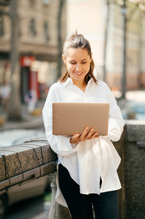 Cheerful young woman is checking up her email from a laptop on a balcony.の写真素材
