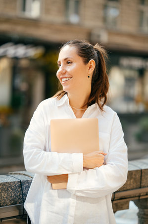 Close up vertical shot of a happy woman embracing her laptop and looking aside.の写真素材