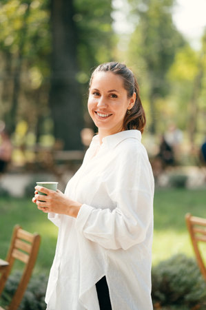 vertical portrait of a young woman wearing white shirt enjoying her coffee.