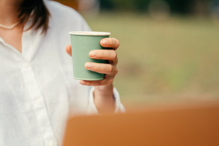 Young woman in white shirt is holding a green paper take away cup of coffee.の写真素材
