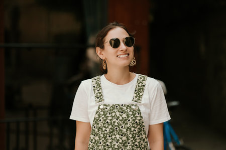 Cheerful young woman is smiling and looking aside while wearing sunglasses.の写真素材