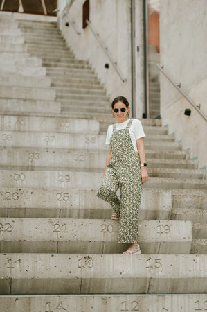 Full length portrait of a young woman in green coming down concrete stairs.