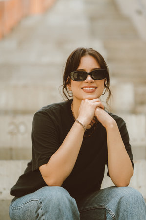 Young confident smiling woman wearing sunglasses is sitting on the stairs.の写真素材