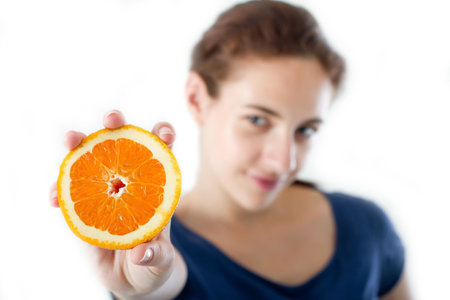 Teen girl holding a sliced orange. Studio shot. Focus on the orange.の写真素材