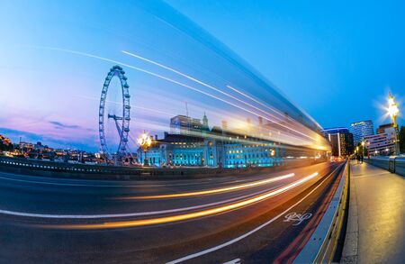 Cityscape of London at blue hour, view from the bridge of Westminster over the eye wheel and car traces on the road, in England, UKの写真素材
