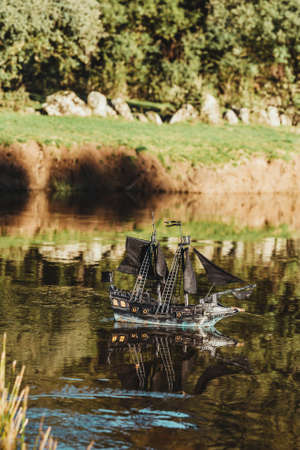 A black toy pirate ship sailing on the river on a summer day in the middle of natureの写真素材