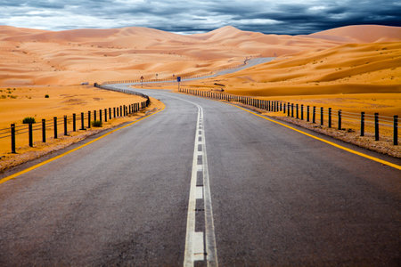 Winding black asphalt road through the sand dunes of Liwa oasis, United Arab Emiratesの写真素材