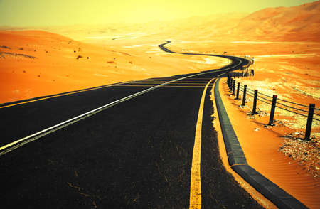 Winding black asphalt road through the sand dunes of Liwa oasis, United Arab Emiratesの写真素材