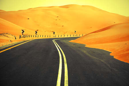 Winding black asphalt road through the sand dunes of Liwa oasis, United Arab Emiratesの写真素材