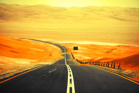 Winding black asphalt road through the sand dunes of Liwa oasis, United Arab Emiratesの写真素材