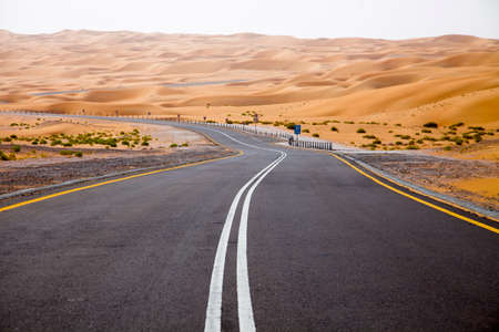Winding black asphalt road through the sand dunes of Liwa oasis, United Arab Emiratesの写真素材