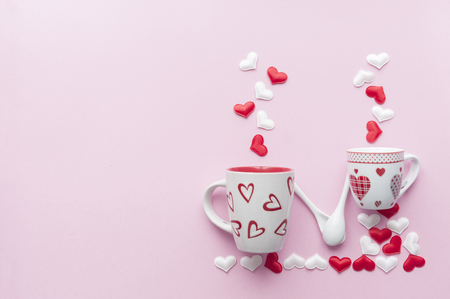 Valentine's day concept: tea and coffee cup holding hand made with spoons on pink baground full of heartsの写真素材