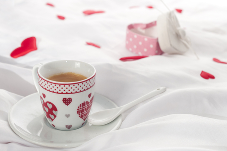 A heart decorated coffee cup on a white table with red hearts and a gift boxの写真素材