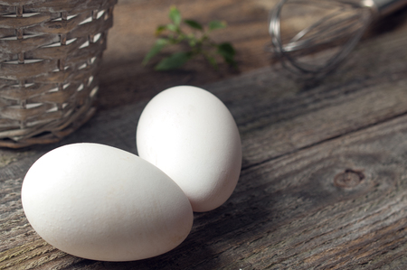 Goose eggs on wooden table with a basket and a whipの写真素材