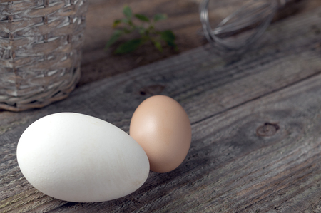 Goose and hen eggs on wooden table with basket and whipの写真素材