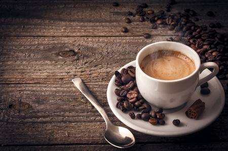 A cup of coffee on old wooden table with some beans a spoon and a stick of cinnamonの写真素材