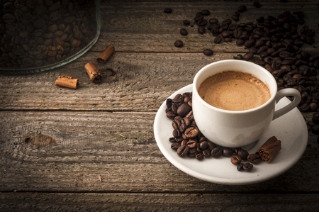 A cup of coffee on old wooden table with some beans and some cinnamon's sticksの写真素材