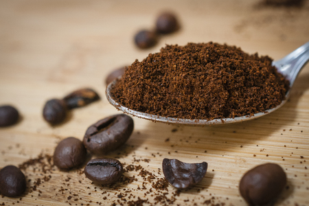 Teaspoon with fresh ground coffee over a wooden table with roasted coffee beansの写真素材