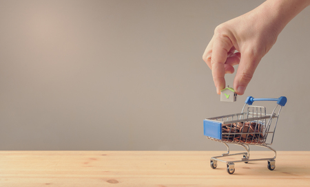 Male hand put a paper house into a cart full of coins, saving and loan or mortgage conceptの写真素材