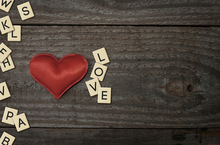 A red fabric heart on a wooden table with plastic letters that forms the word loveの写真素材