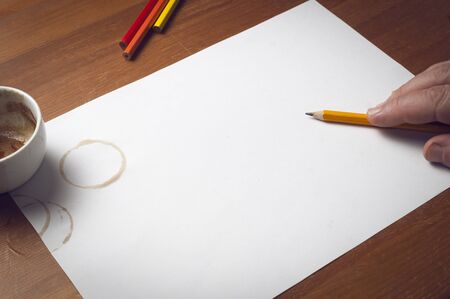 Man hold a pencil over a white sheet of paper, pencils, offee cup and coffee stains as decorationの写真素材