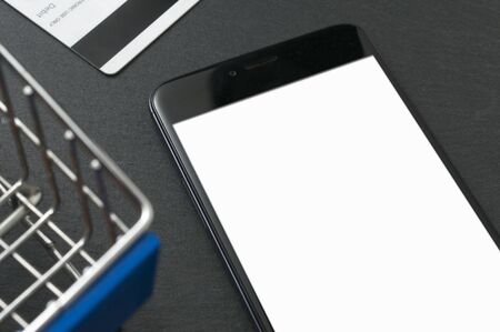 Online shopping concept: blank screen smartphone on a table near to a toy shopping cart and a debit card.の写真素材