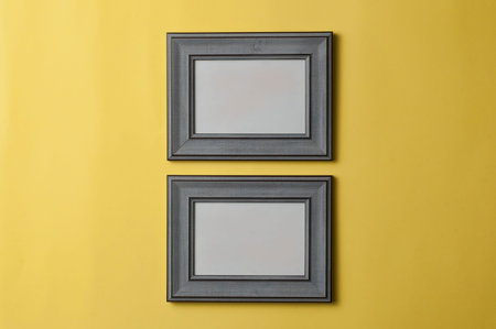 Two blank grey wooden photo frames hanging from a yellow wall