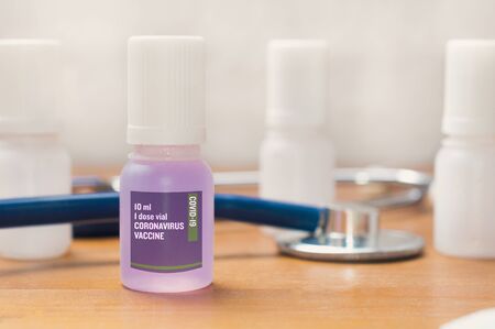 Coronavirus vaccine concept: vial of a coronavirus test vaccine on a wooden table with a stethoscope and some empty vialsの写真素材
