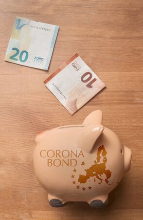 Coronabond concept: a piggybank with a map of Europe and the text coronabond printed on in on a wooden table with some euro bills. の写真素材