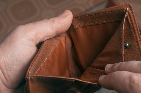 Man shows the empty interior of a brown leather wallet during a period of economic crisis