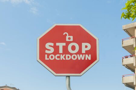 Stop lockdown concept: a stop street sign with the text stop lockdown with a blue sky on the background and some houses and trees aroundの写真素材